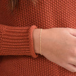 Close-up of a person wearing a rust-colored sweater and a gold bracelet.