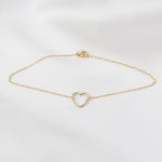 Gold bracelet with a heart-shaped clasp on a light gray background