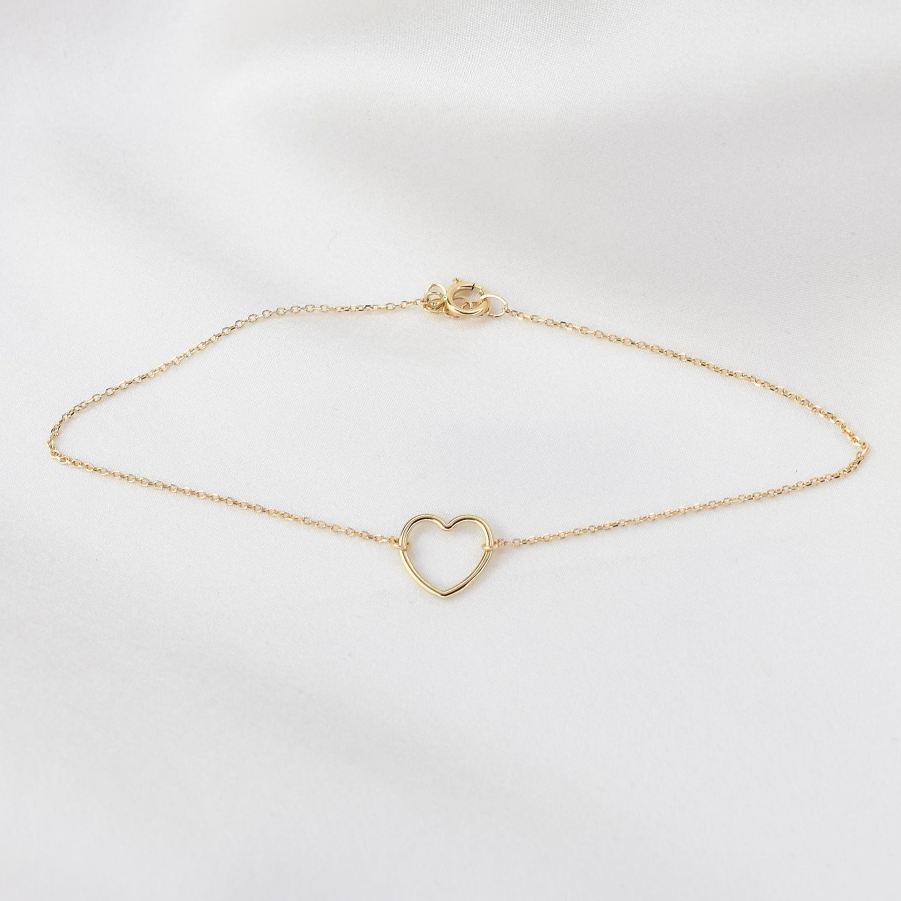 Gold bracelet with a heart-shaped clasp on a light gray background