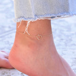 Gold heart-shaped anklet on a person's ankle with denim jeans.