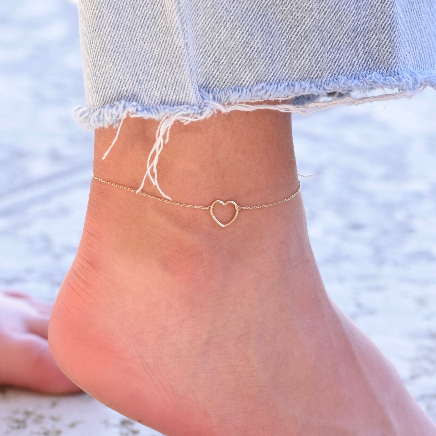 Gold heart-shaped anklet on a person's ankle with denim jeans.