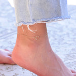 Ankle with a gold heart-shaped anklet on a blurred beach background