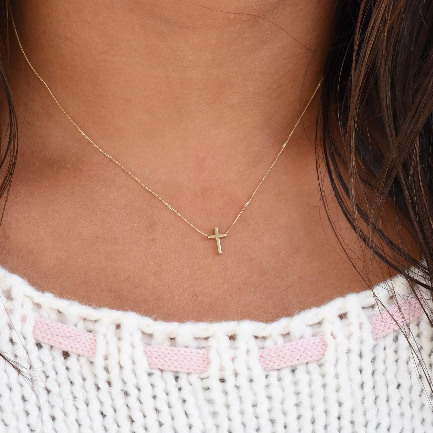 Gold cross necklace on a person wearing a white and pink textured top