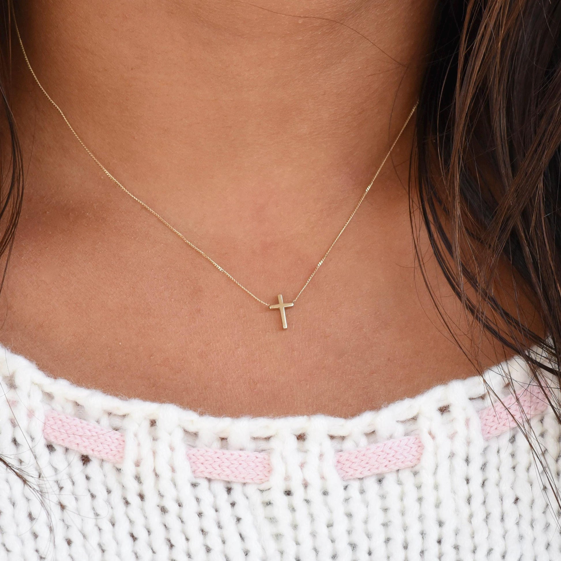Gold cross necklace on a person wearing a white and pink textured top