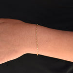 Gold bracelet on a wrist against a black background