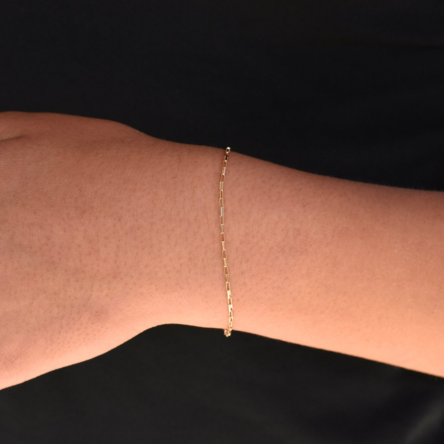 Gold bracelet on a wrist against a black background