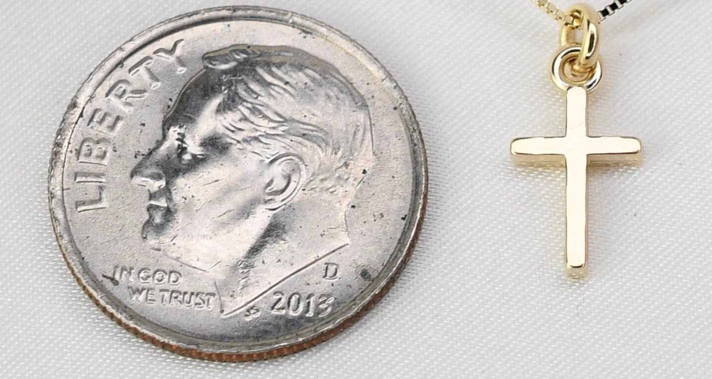 Gold cross pendant next to a quarter on a white background