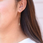 Close-up of a person wearing a gold cross earring.