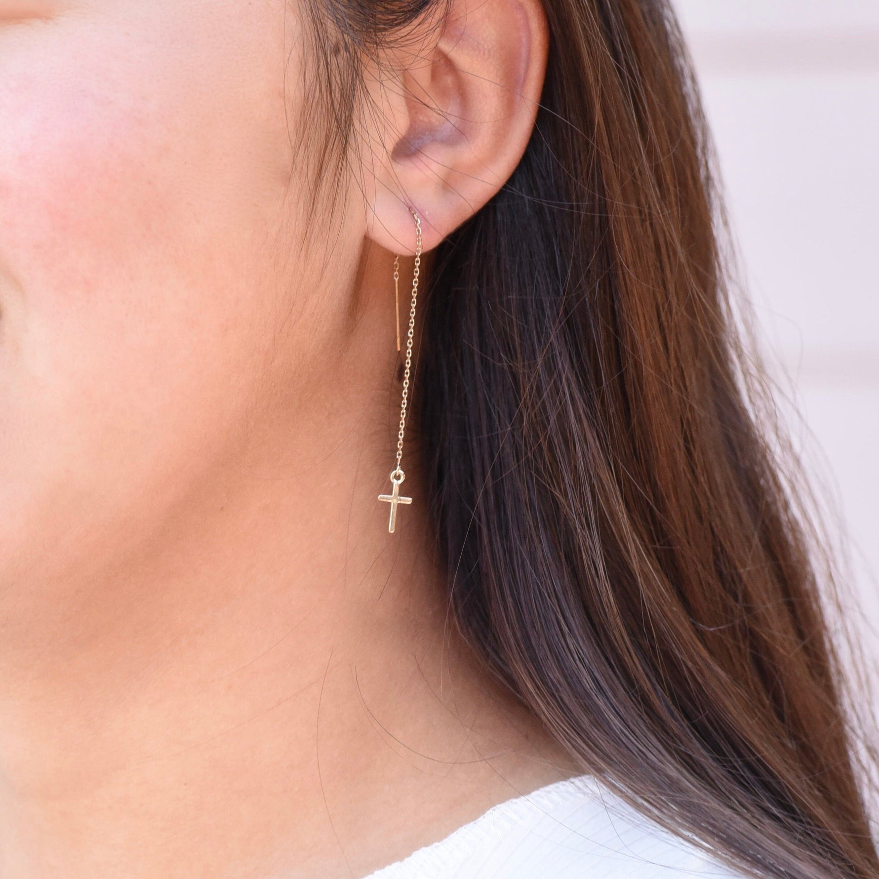 Close-up of a person wearing a gold cross earring.