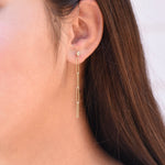 Gold bar earring worn by a person with long brown hair.