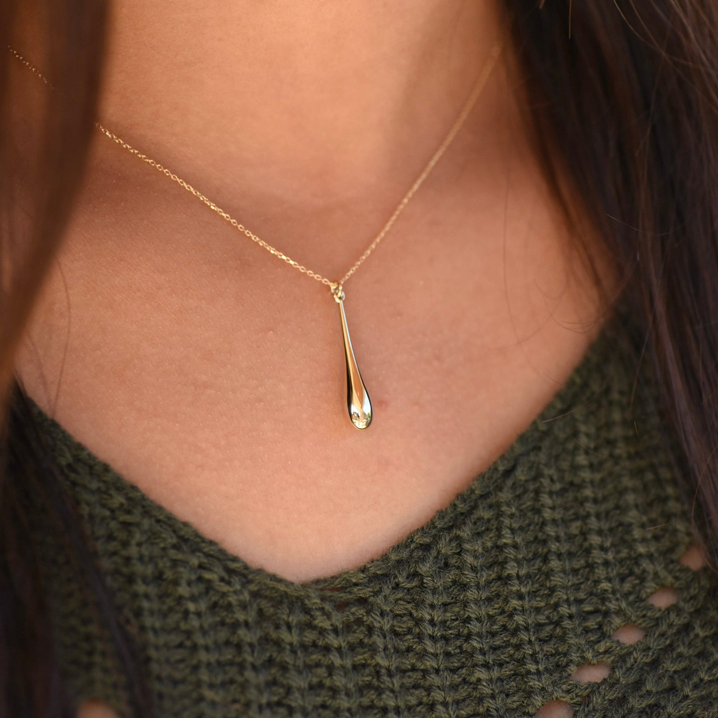 Gold necklace with a pendant worn by a person in a green sweater.