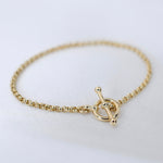 Gold bracelet with a toggle clasp on a light background