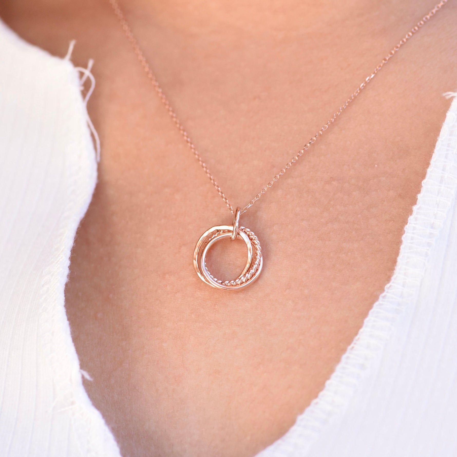 Rose gold necklace with a double-circle pendant on a person wearing a white top.