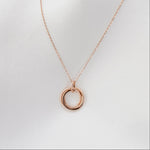 Rose gold necklace with a circular pendant on a light gray background