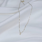 Delicate gold necklace with a small pendant on a white fabric background