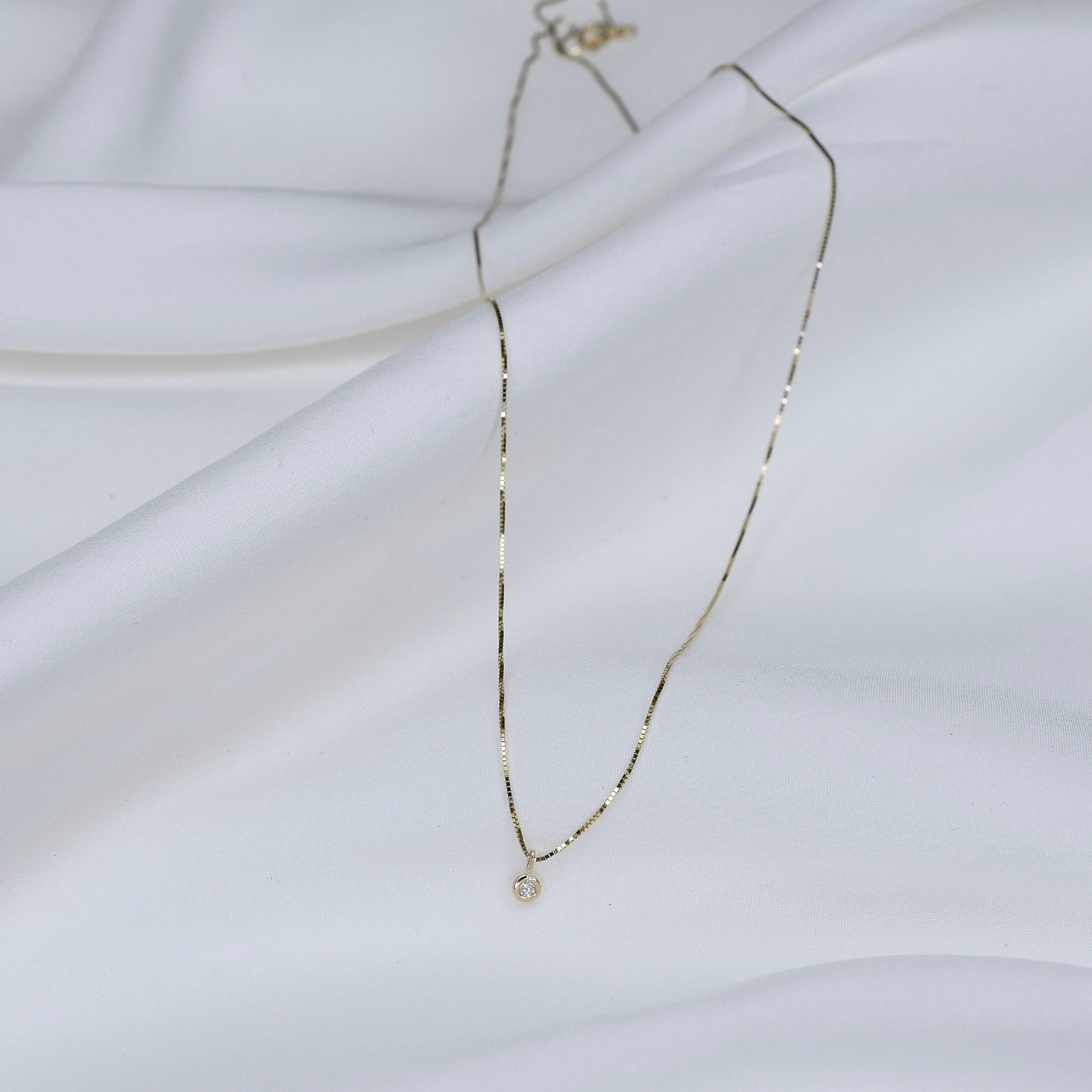 Delicate gold necklace with a small pendant on a white fabric background