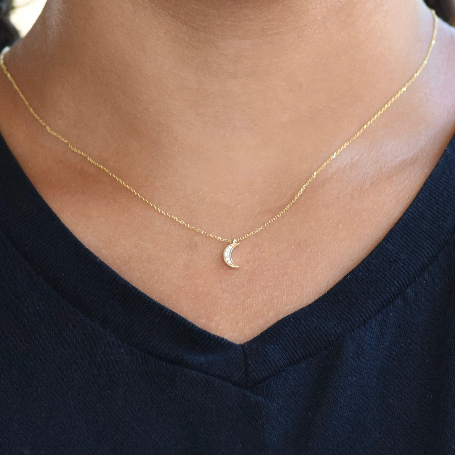 Gold necklace with a small crescent moon pendant on a person wearing a black top.