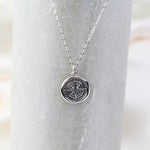 Silver necklace with a compass pendant on a marble surface