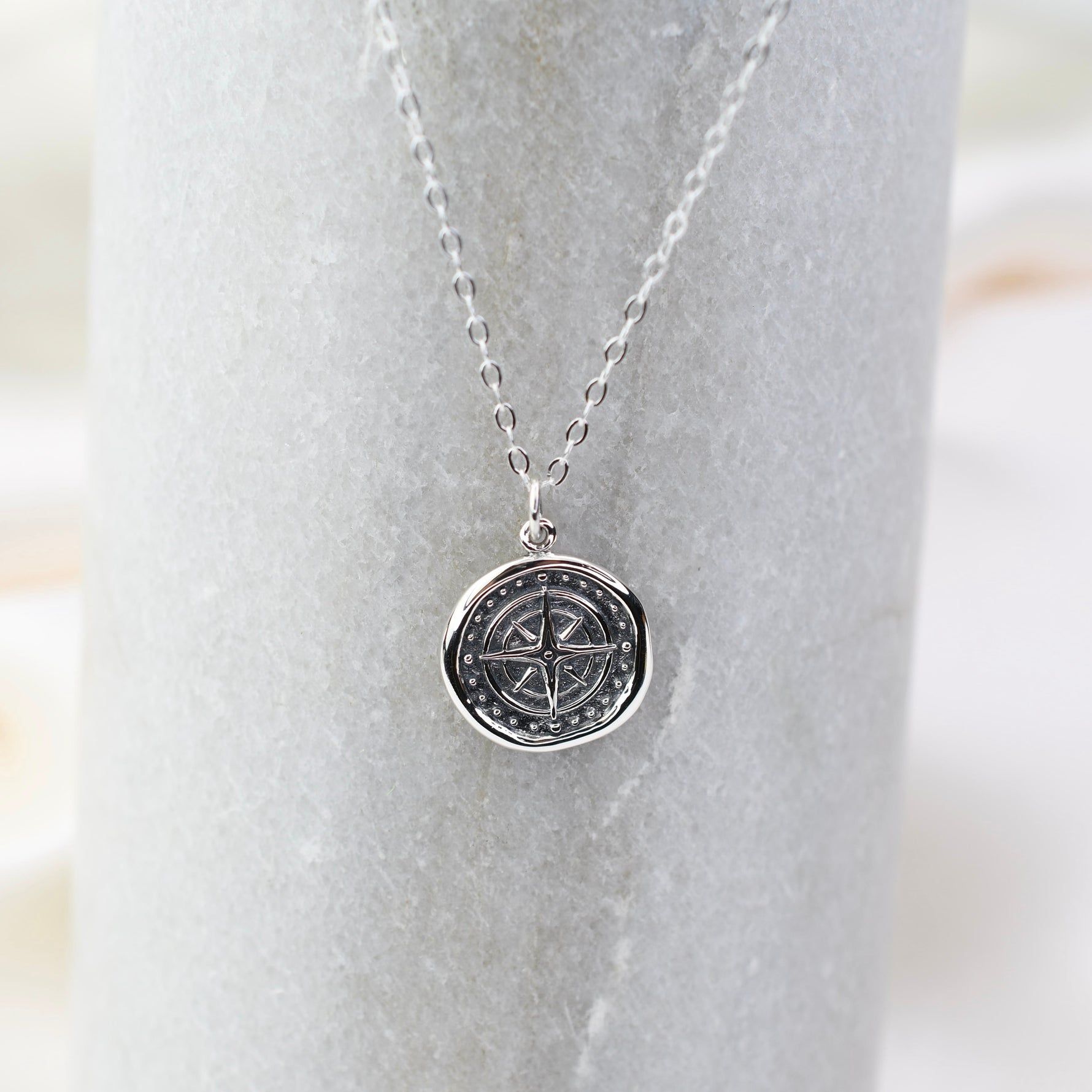 Silver necklace with a compass pendant on a marble surface