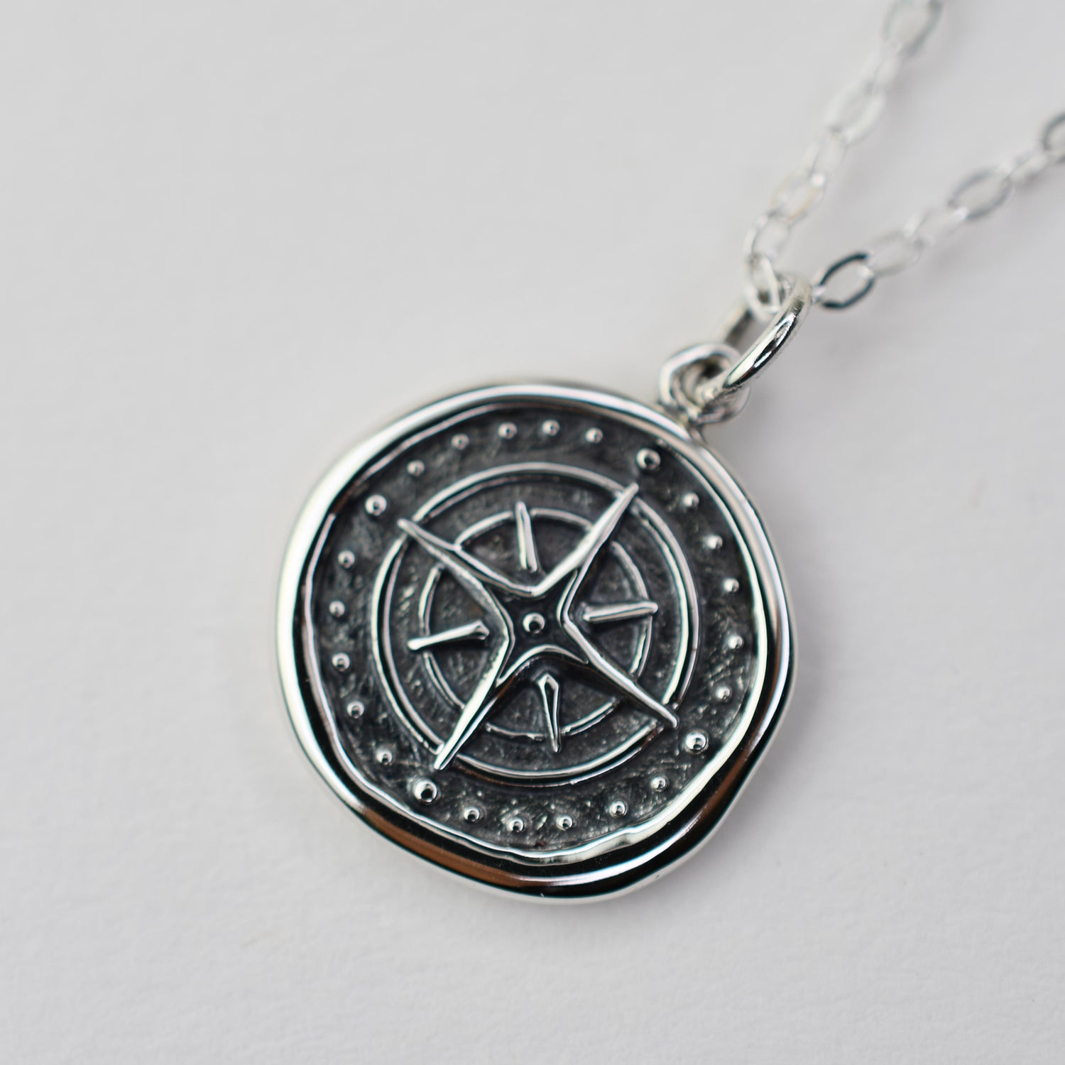 Silver pendant with star design on a light gray background
