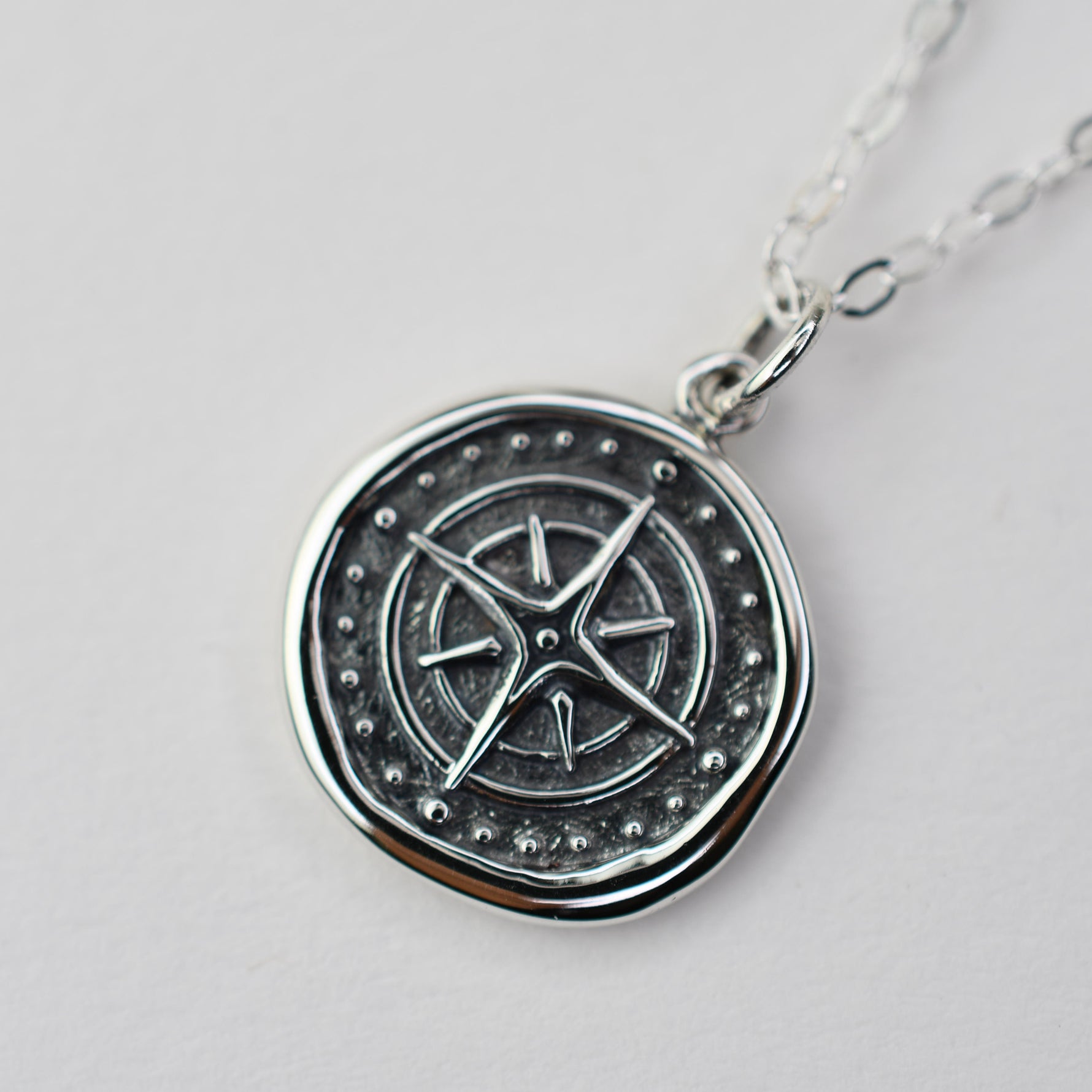 Silver pendant with star design on a light gray background