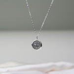 Silver necklace with a compass pendant on a neutral background