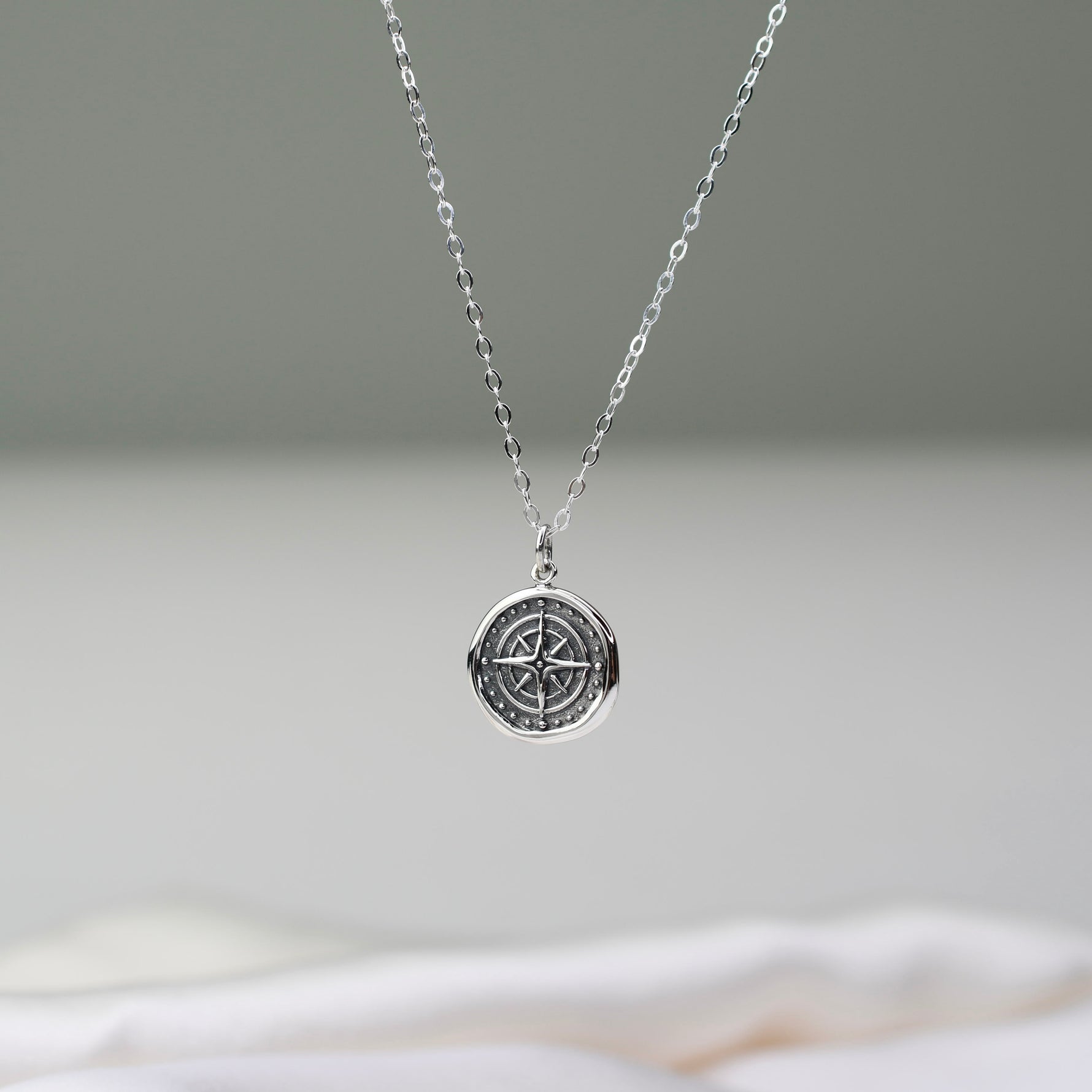 Silver necklace with a compass pendant on a neutral background