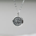 Silver necklace with a compass pendant on a neutral background