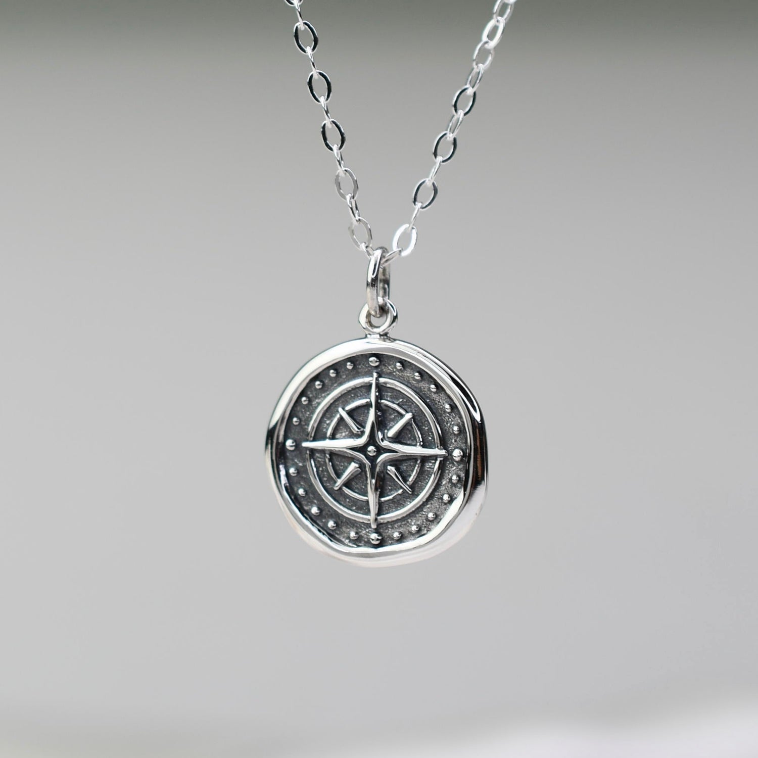 Silver necklace with a compass pendant on a neutral background