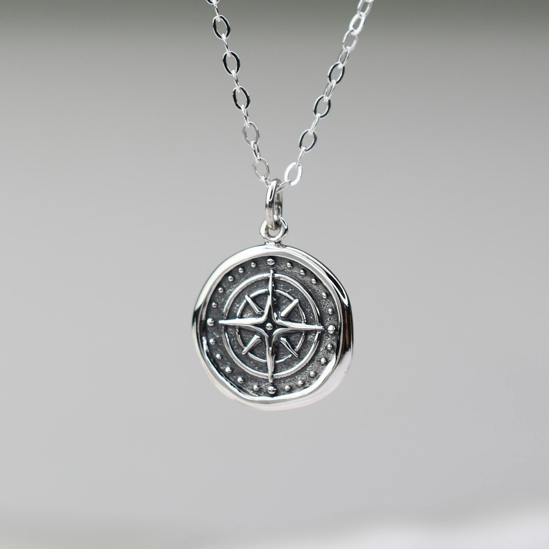 Silver necklace with a compass pendant on a neutral background