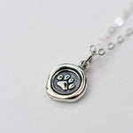 Silver necklace with a paw print pendant on a light gray background
