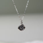 Silver necklace with a round pendant on a gray background