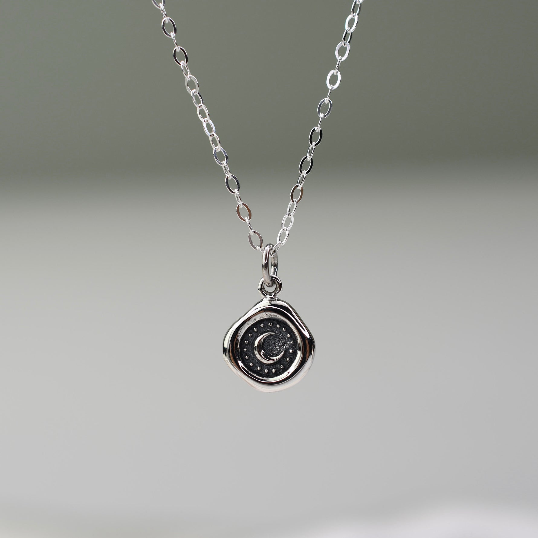 Silver necklace with a round pendant on a gray background
