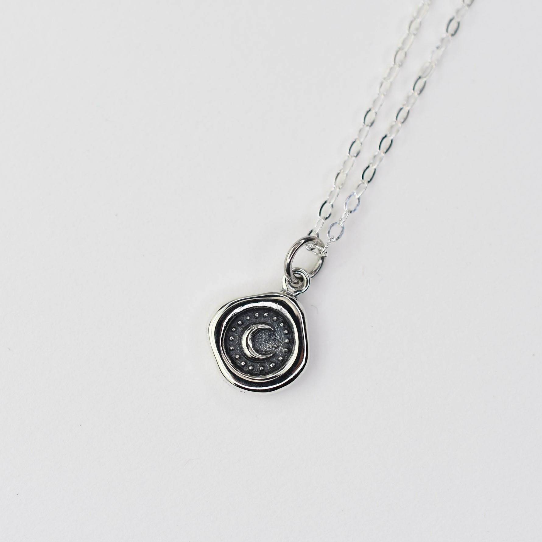 Silver necklace with a circular pendant on a light gray background