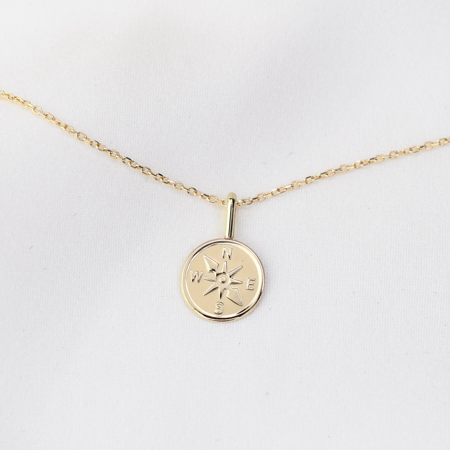 Gold necklace with a compass pendant on a white background