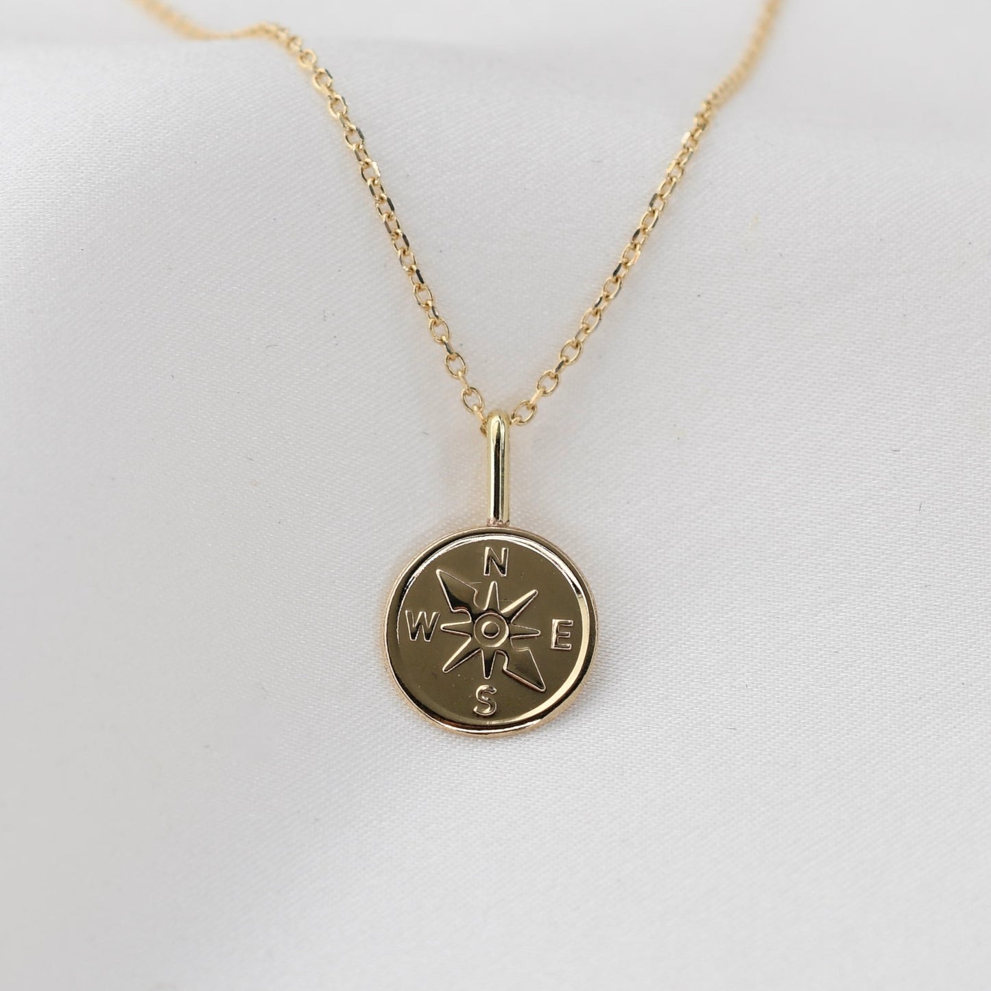 Gold necklace with a compass pendant on a white background