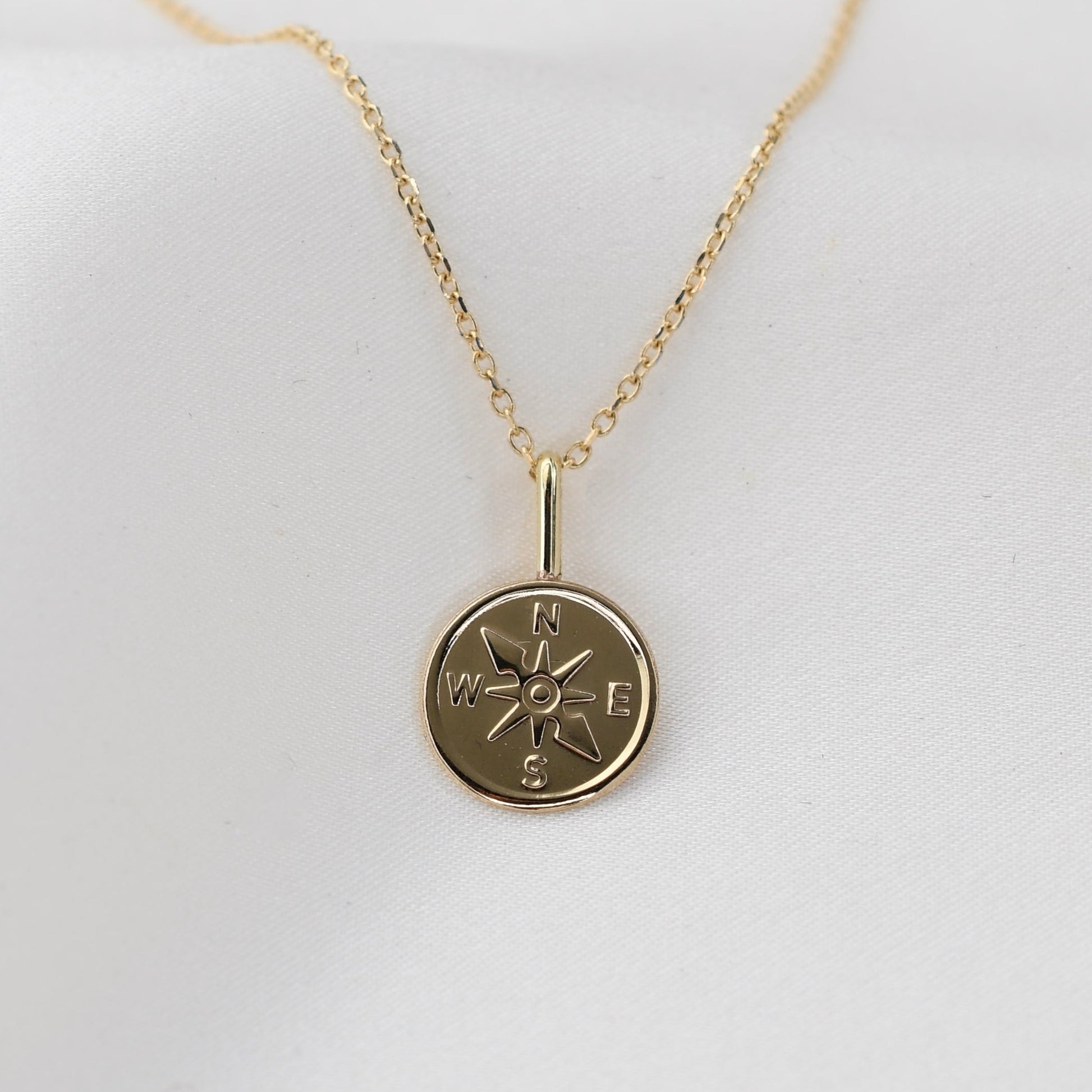 Gold necklace with a compass pendant on a white background
