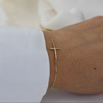 Gold bracelet with a cross on a wrist against a white background