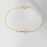 Gold bracelet with a small cross pendant on a light gray background