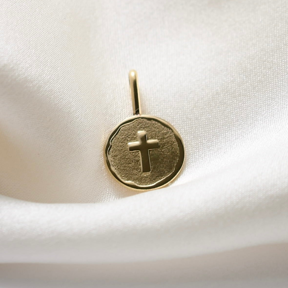 Gold pendant with a cross on a white satin background