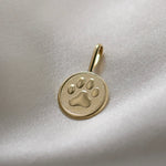 Gold pendant with a paw print design on a light fabric background