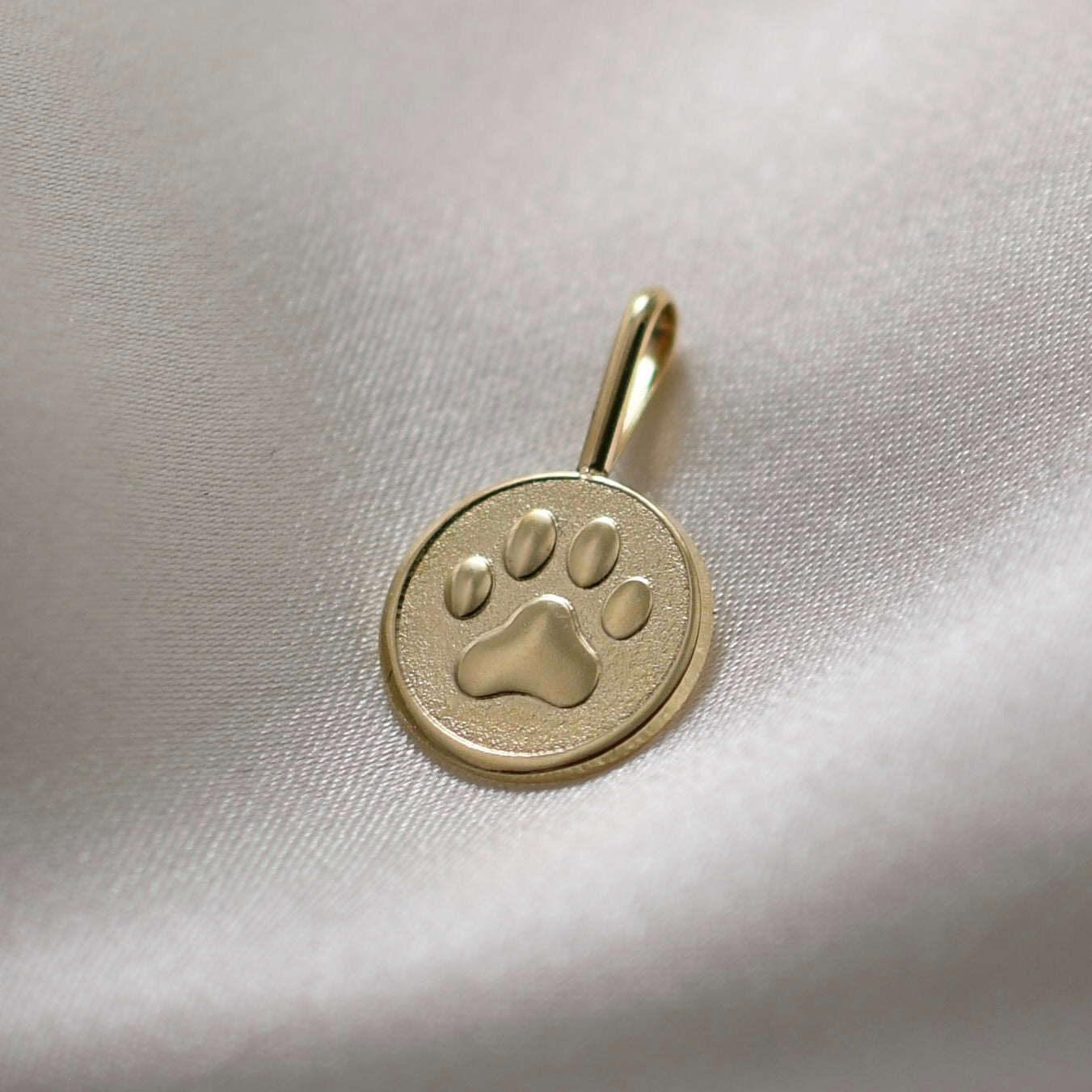 Gold pendant with a paw print design on a light fabric background
