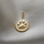 Gold pendant with a paw print design on a light gray fabric background