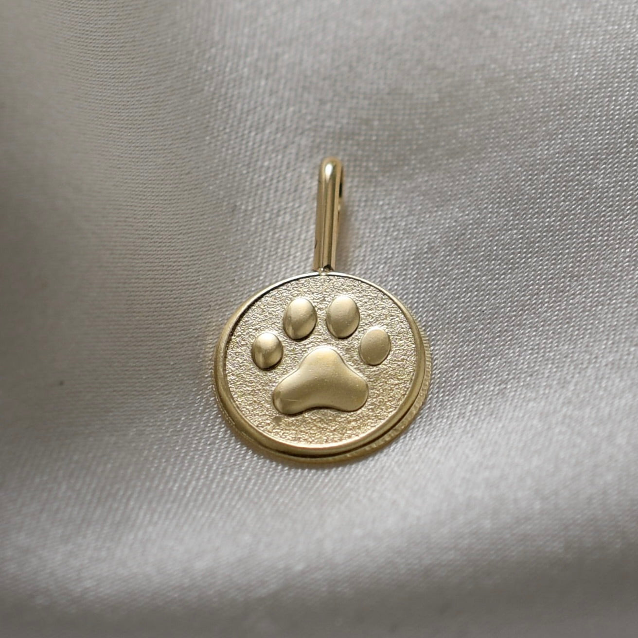 Gold pendant with a paw print design on a light gray fabric background