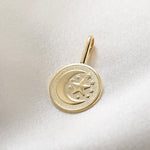 Gold pendant with moon and star design on a white fabric background