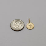 Gold cross pendant next to a silver quarter on a gray background