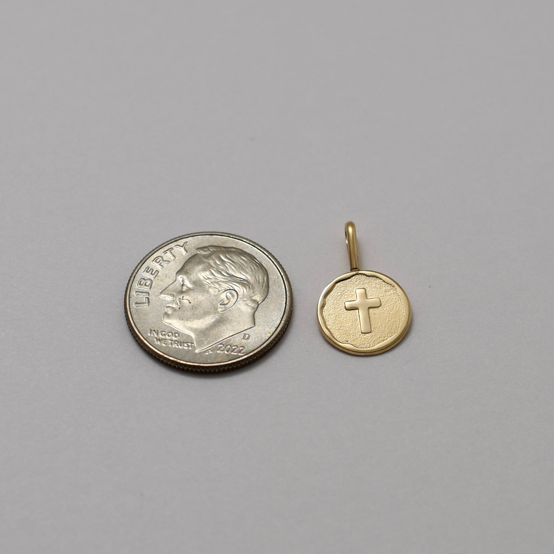 Gold cross pendant next to a silver quarter on a gray background