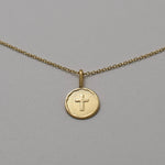 Gold necklace with a round pendant featuring a cross on a gray background
