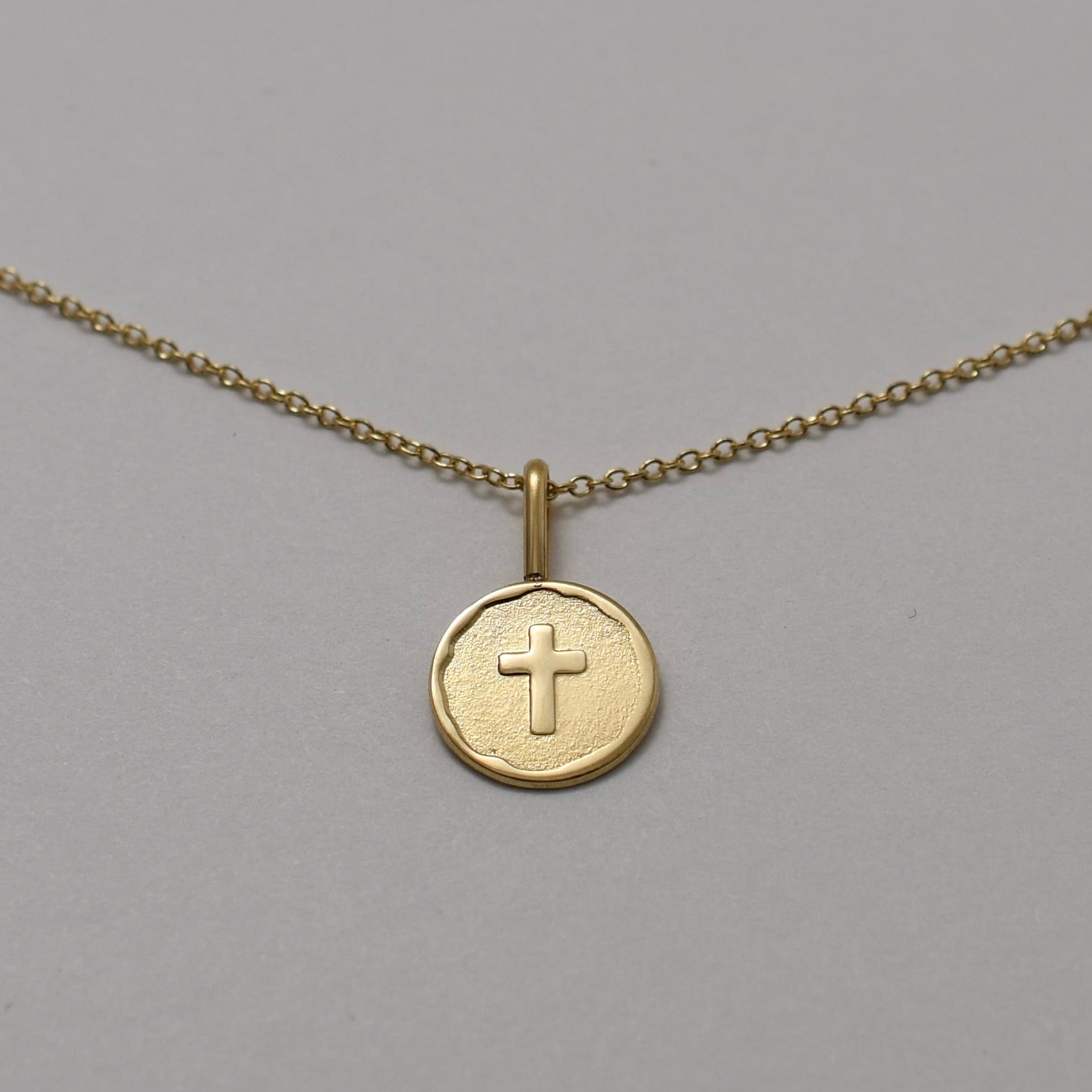 Gold necklace with a round pendant featuring a cross on a gray background