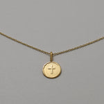 Gold necklace with a round pendant featuring a cross on a gray background